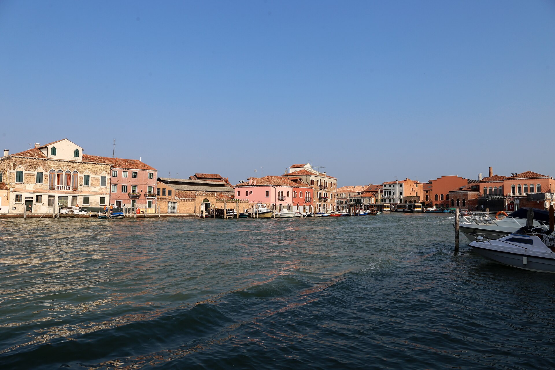 A canal on Murano with boats moored along brick houses